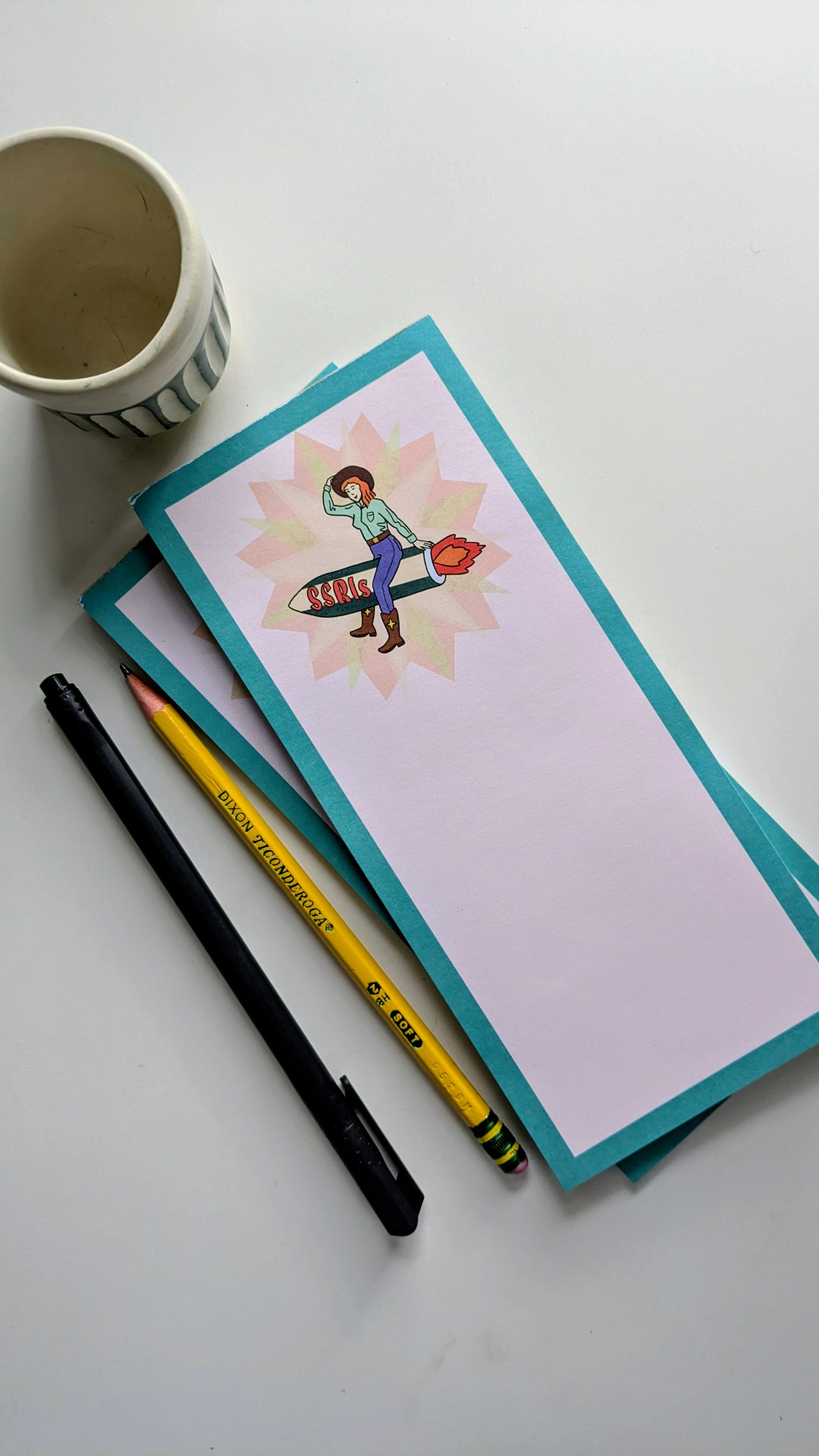 Notepad with a colorful illustration, pencil, and pen on a white surface