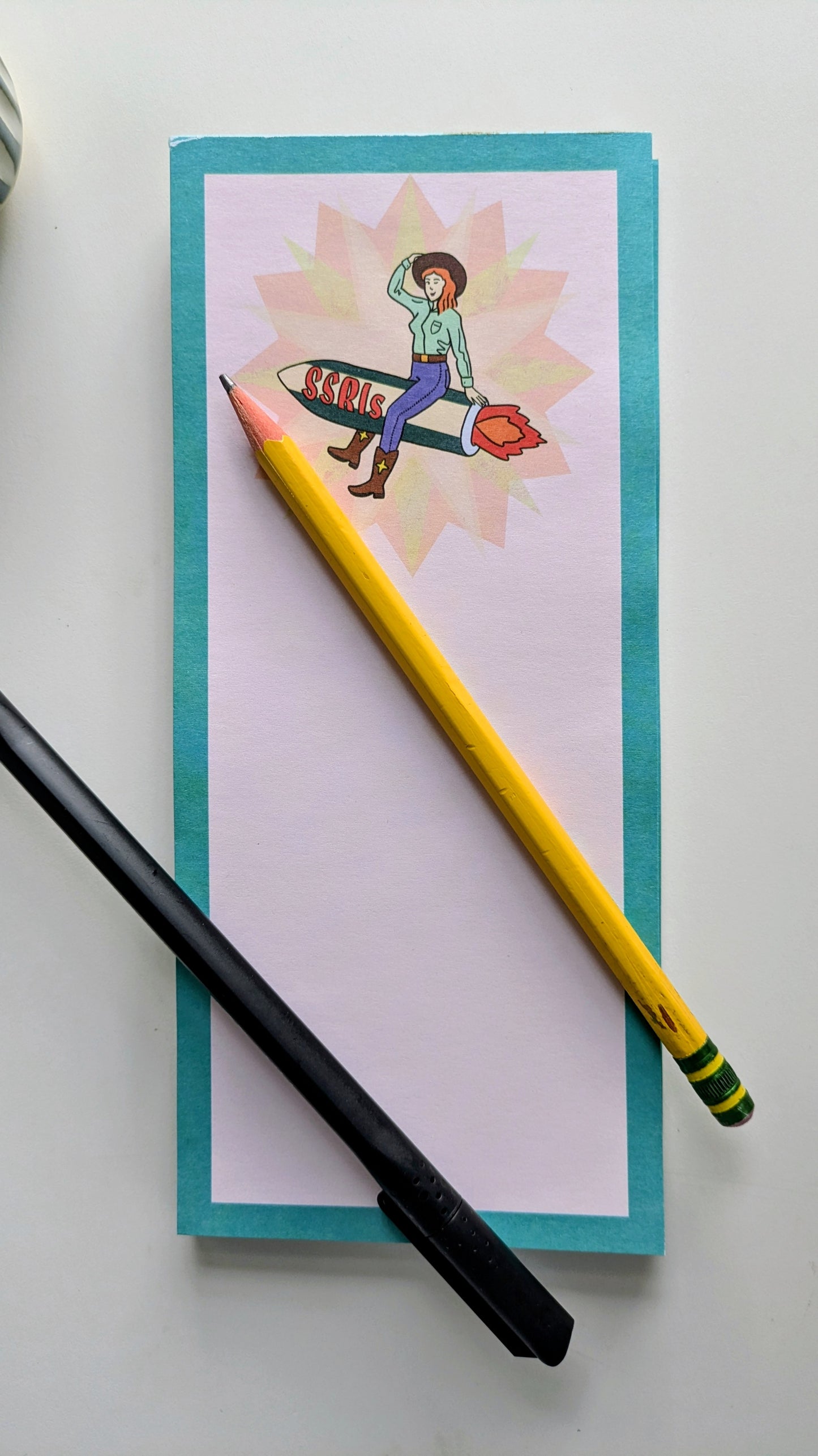 Notebook with a colorful illustration, a yellow pencil, and a black pen on a white background