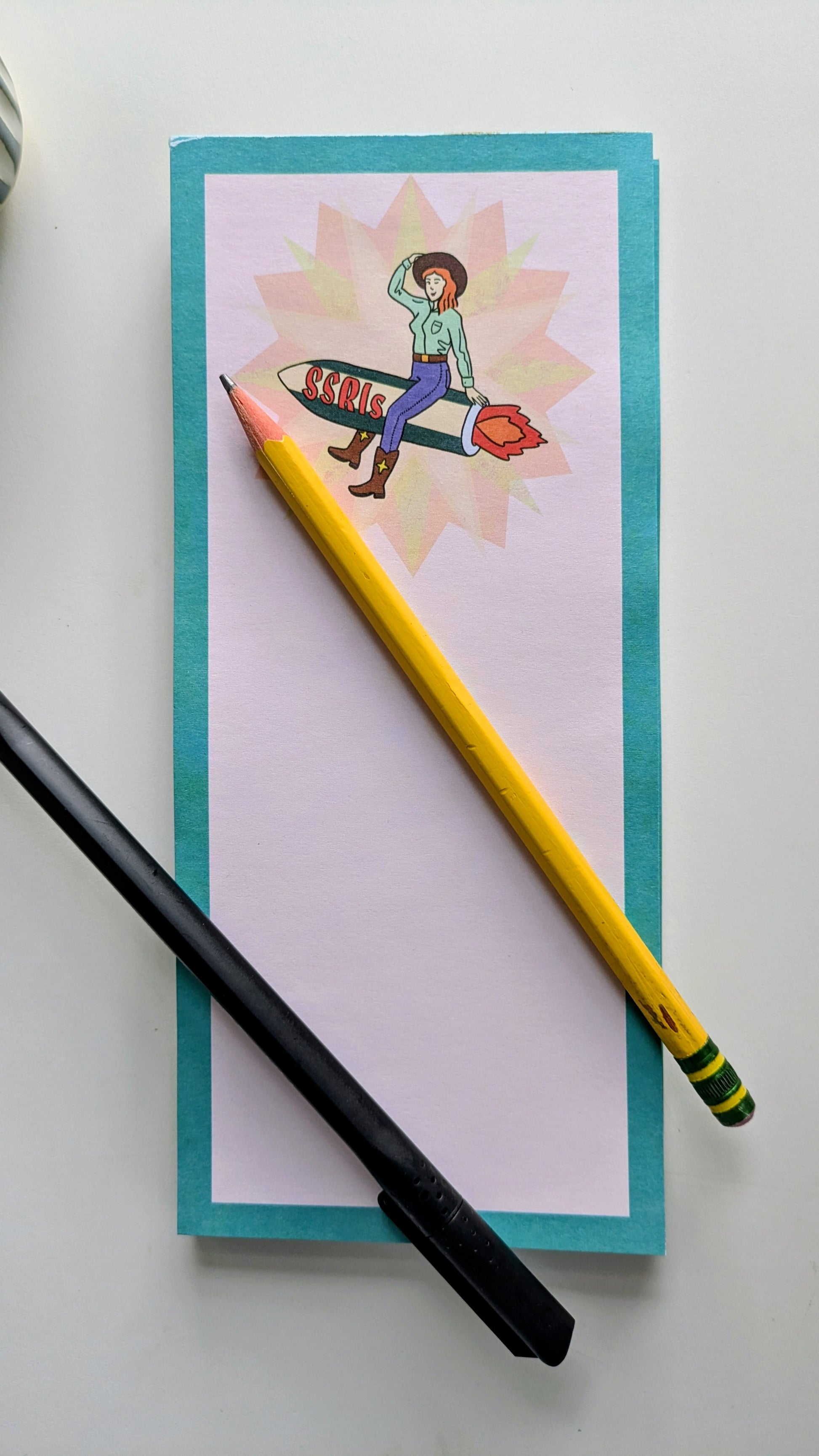 Notebook with a colorful illustration, a yellow pencil, and a black pen on a white background