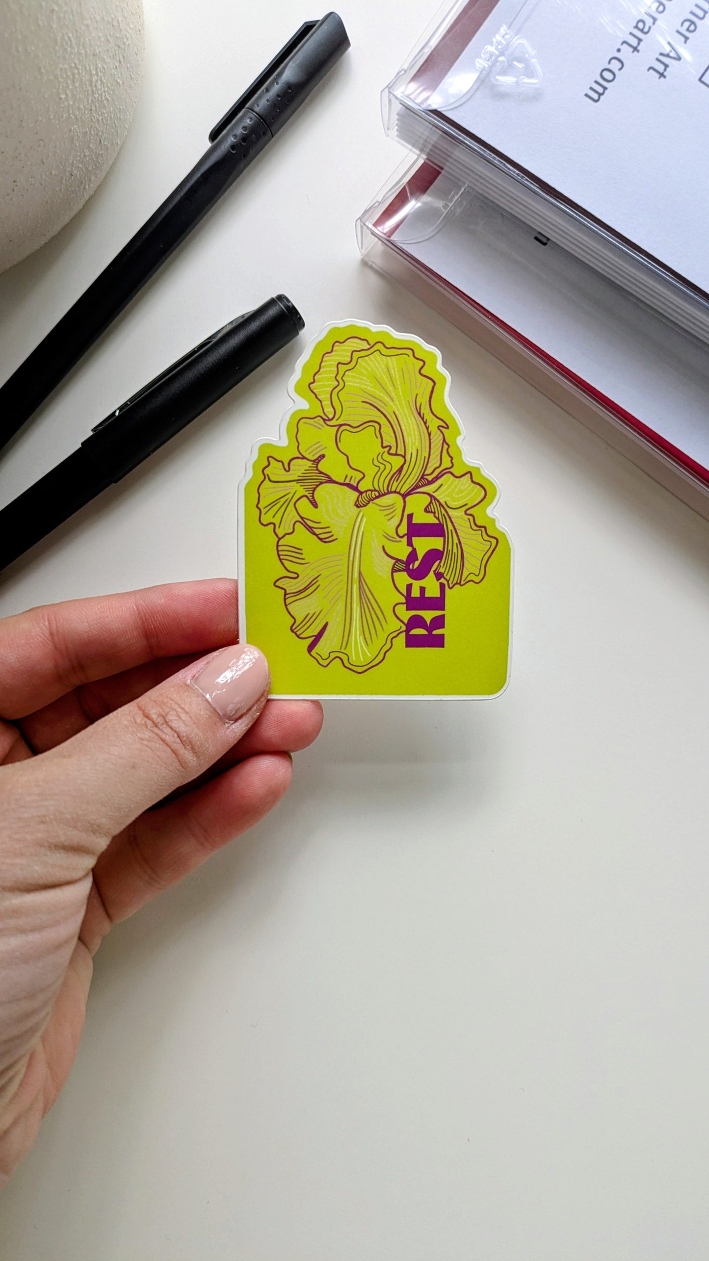 Rest floral sticker held by a hand next to notecard sets