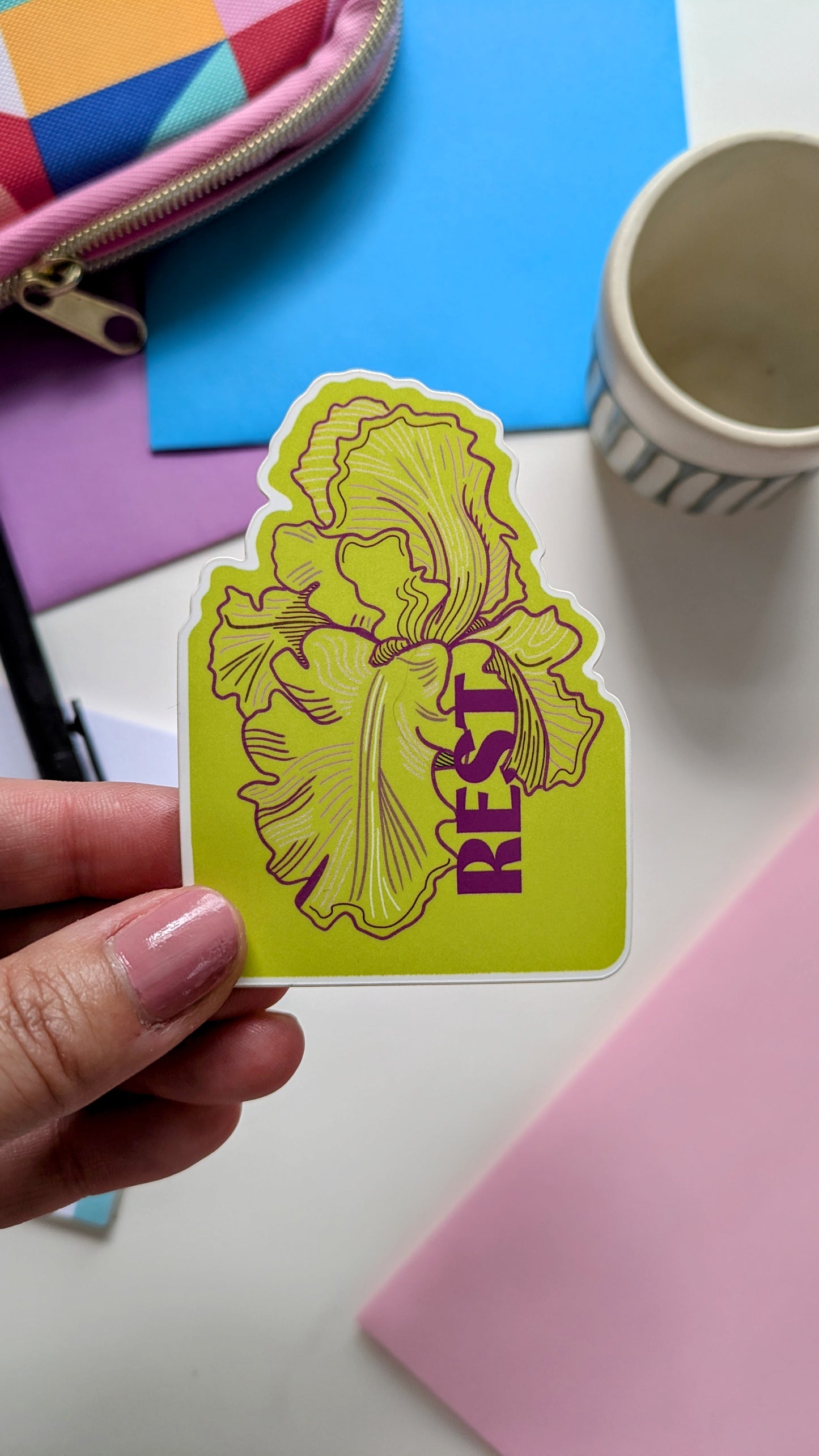 Rest floral sticker held by a hand above envelopes and stationery